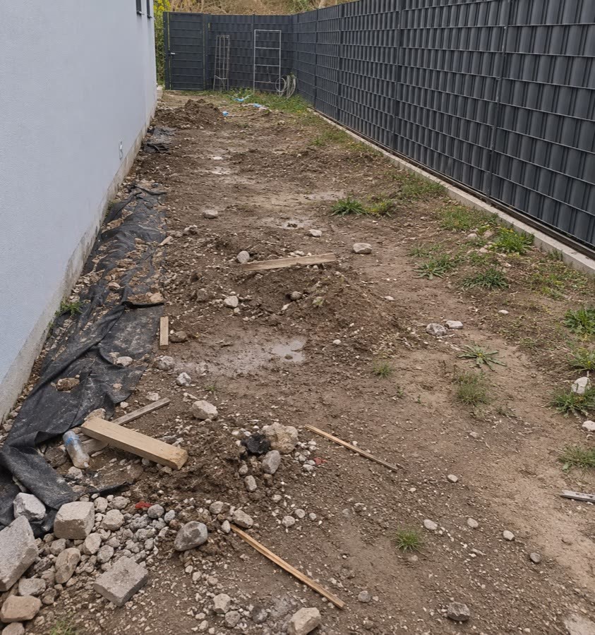 Derselbe Gartenweg vor dem Pflastern: unbefestigter Untergrund entlang des Zauns